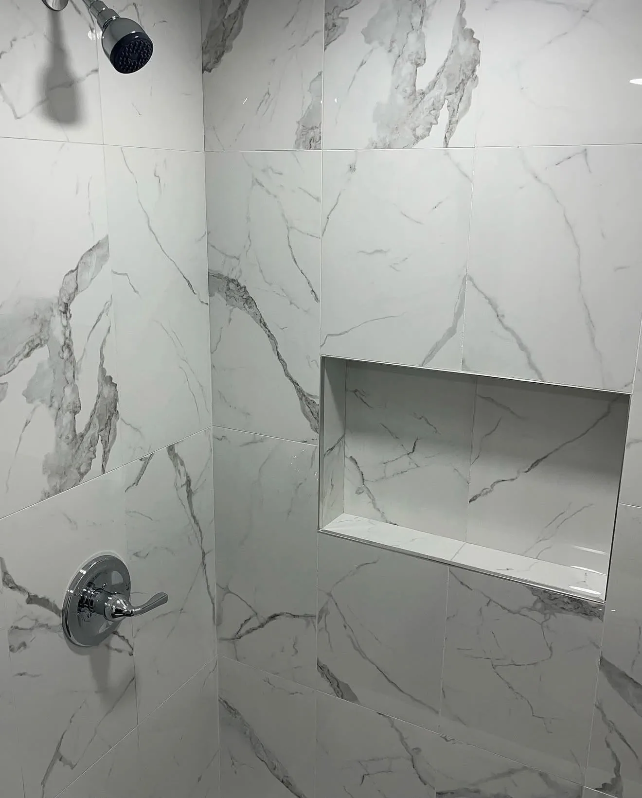 Chrome shower head and valve on marble-look tile with recessed niche